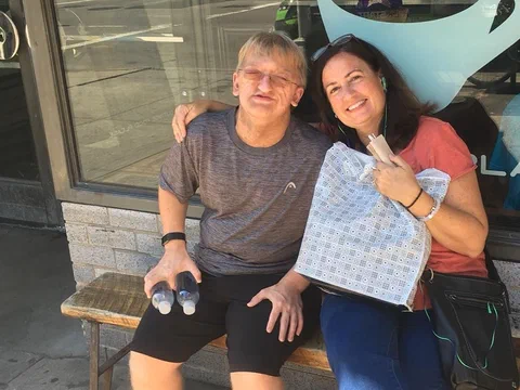 Alex and his mother sitting on a bench outside a shop, holding a gift bag