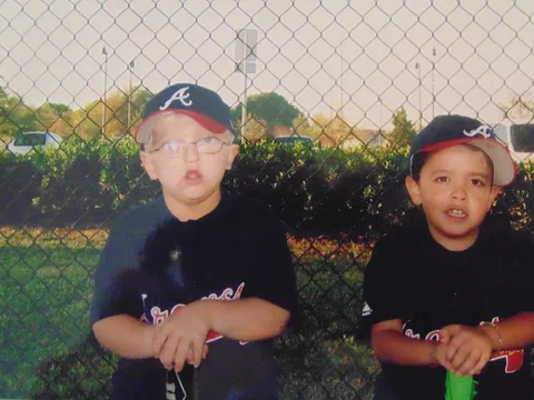 Alex and a teammate in baseball uniforms posing by a fence