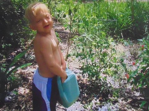 Alex as a toddler watering a garden with a blue watering can