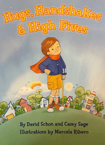 Cover of Hugs, Handshakes & High Fives: Travis, a boy in a red cape, gives a thumbs up on a hill above a town