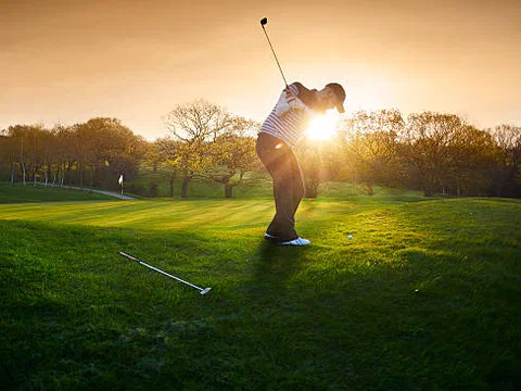 A golfer chipping onto a green, backlit by the morning sun