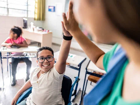 A student who uses a wheelchair giving a high five to a classmate in a school hallway