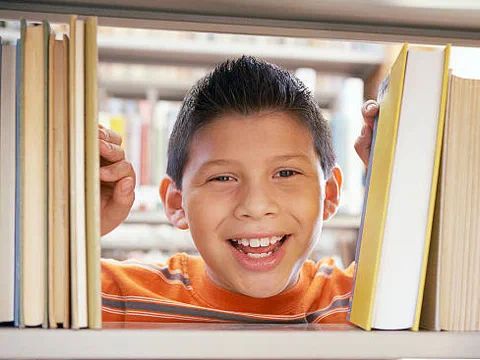 A smiling boy peeking between shelves of books in a library