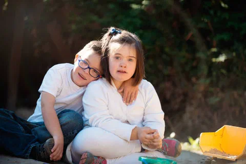 A young girl hugging her brother, who has Down syndrome, outdoors