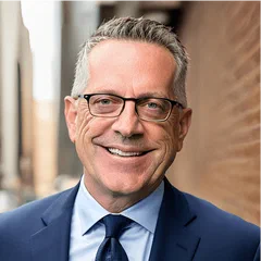 Dave Schon smiling in a suit and glasses outdoors